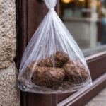 Sachet de déjections canines accroché à une porte en centre-bourg de Chaudes-Aigues