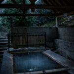 Lavoir ancien de Chaudes-Aigues, bassin en pierre sous une structure en bois, photographié dans une ambiance sombre.