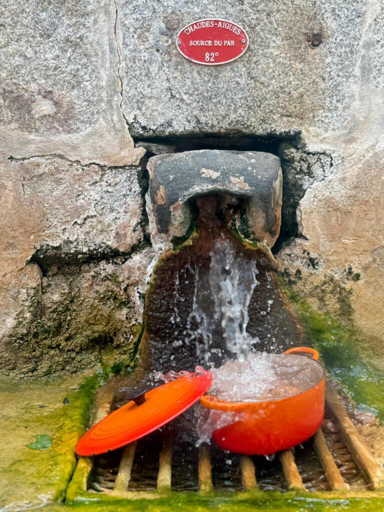 Source du Par à Chaudes-Aigues avec une cocotte placée sous le flux d'eau chaude naturelle à 82 °C pour la cuisson des œufs.
