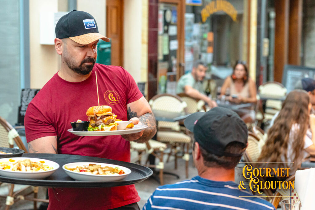 Loïc, alias Simon, servant un burger en terrasse chez Gourmet & Glouton à Chaudes-Aigues